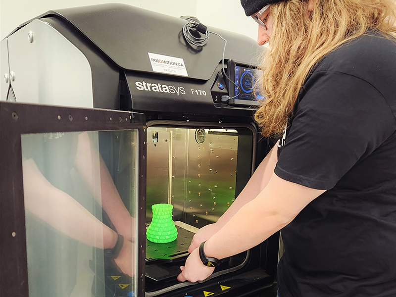 A student retrieves an item from the inside of a 3D printer