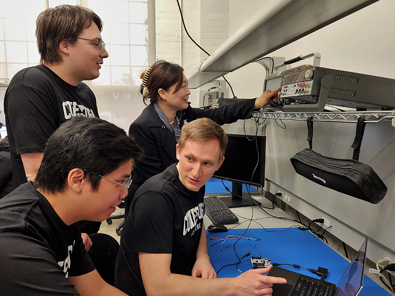 A researcher points at equipment while students look at a laptop