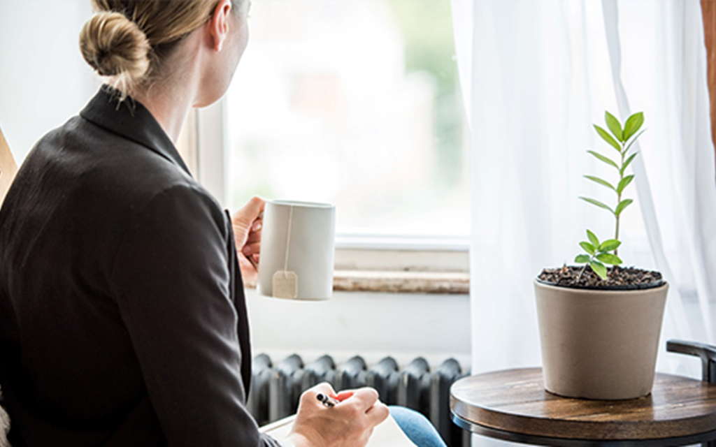 A person looking out the window with a mug in their hand