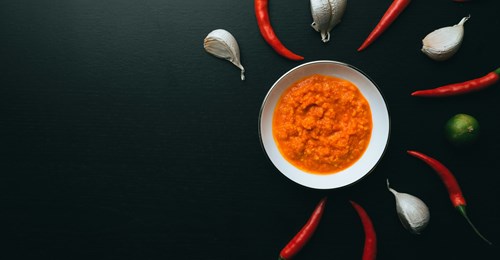 A series of chili peppers and garlic around a bowl of sauce