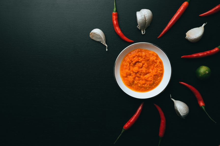 A series of chili peppers and garlic around a bowl of sauce