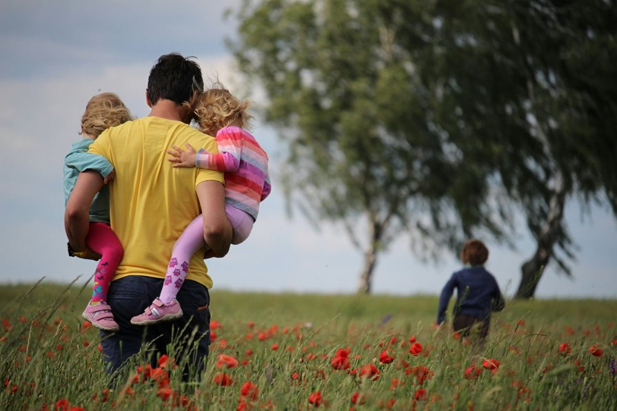 A father holding his two children while one runs ahead