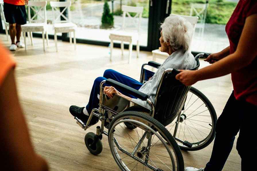 A senior in a wheelchair gets pushed by a nurse