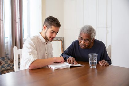 A young person reads along with a senior 