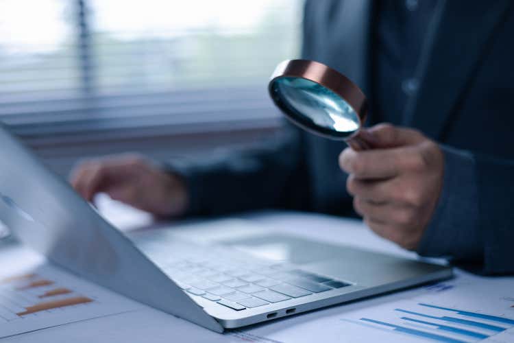 Close-up of a hand holding a magnifying glass over a laptop.
