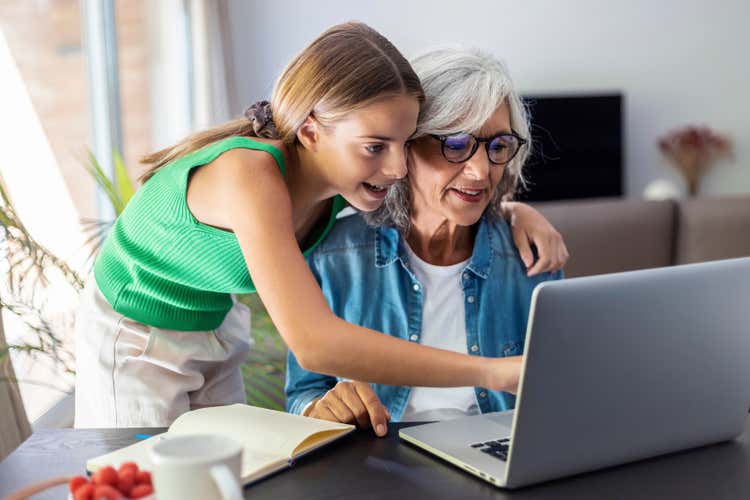 A child and a senior looking at a laptop together.