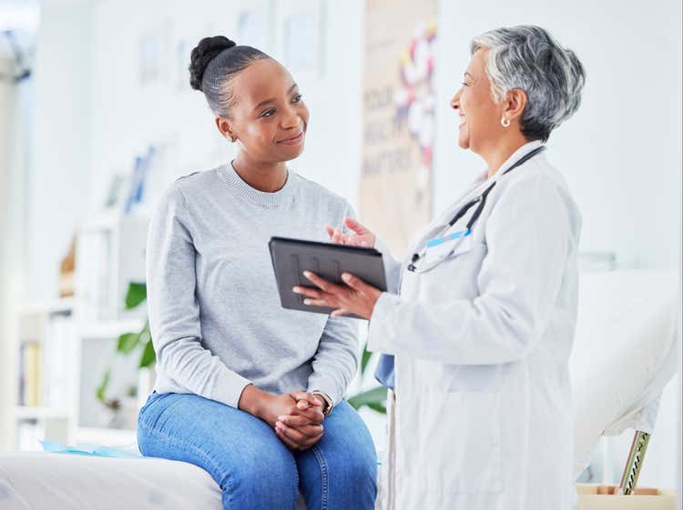 A doctor speaking with a patient sitting on a bed.
