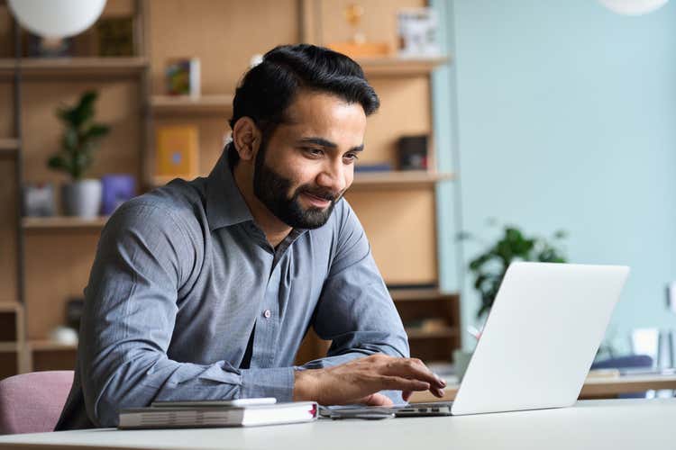 Man sitting and looking at a laptop smiling.